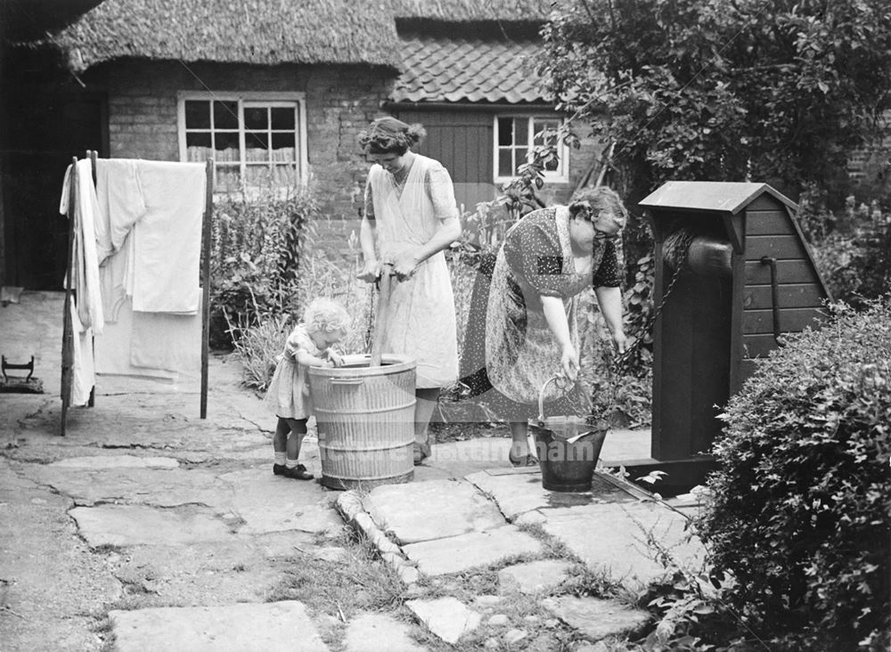 A family in the garden of a timber-framed thatched cottage, Clifton Village, 1948